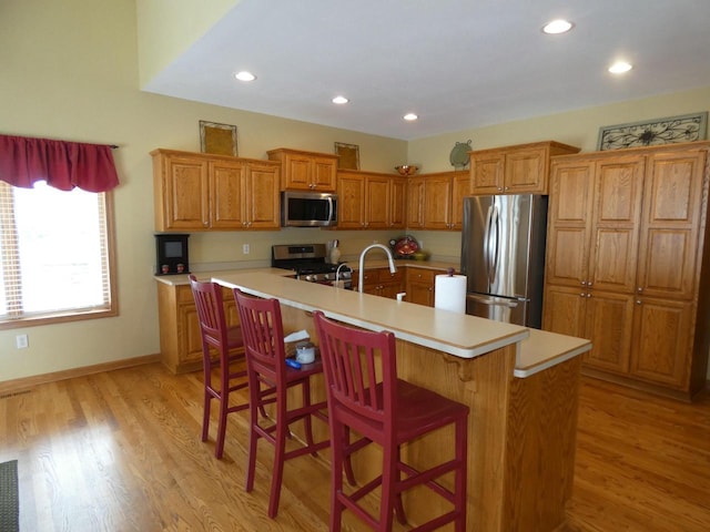 kitchen with light countertops, a breakfast bar area, brown cabinets, and stainless steel appliances