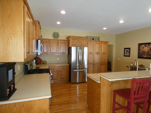 kitchen with a kitchen breakfast bar, stainless steel appliances, light countertops, and light wood-style floors