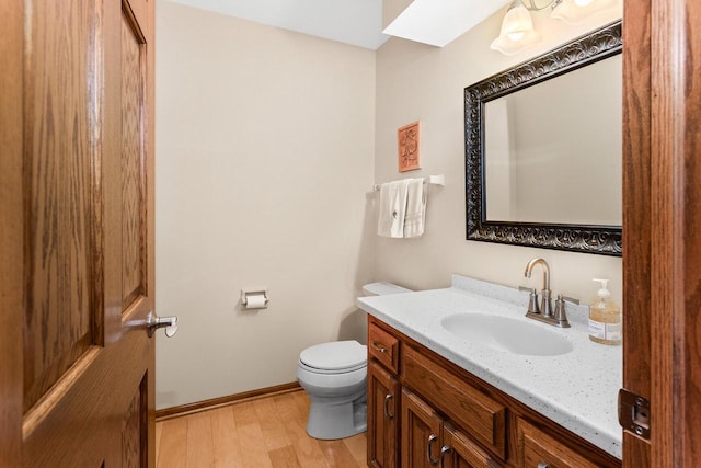 bathroom with vanity, toilet, wood finished floors, and baseboards