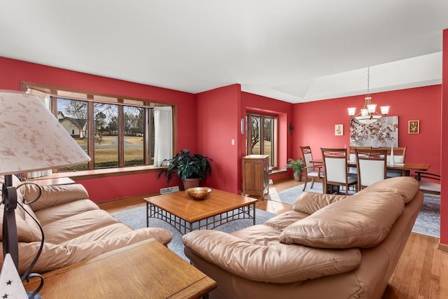 living room featuring a notable chandelier, light wood-style floors, a baseboard radiator, and a healthy amount of sunlight