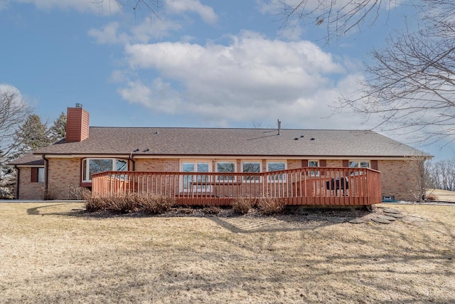 back of house with brick siding, a shingled roof, a chimney, a yard, and a deck