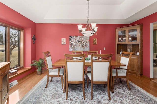 dining space with a tray ceiling, light wood-style flooring, and a chandelier