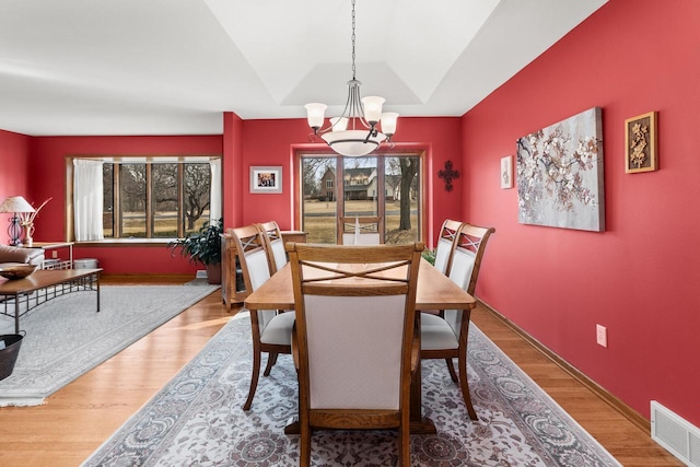 dining area with a chandelier, visible vents, a tray ceiling, and wood finished floors