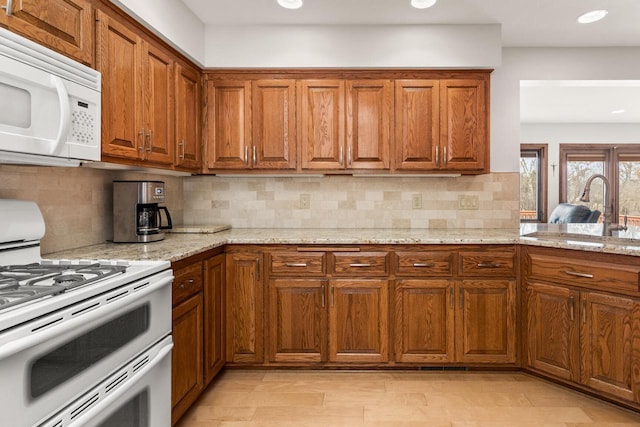 kitchen featuring light stone counters, brown cabinets, white appliances, and a sink