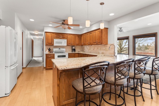 kitchen with brown cabinetry, white appliances, a peninsula, and a ceiling fan