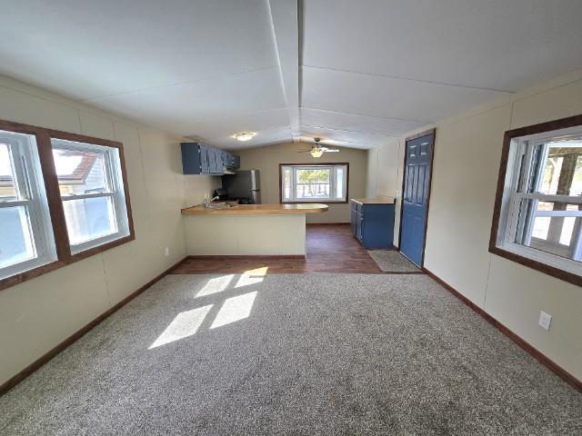 W5029 N Pathfinder Cir, Shawano, WI 54166 - unfurnished living room featuring dark colored carpet, baseboards, ceiling fan, and vaulted ceiling