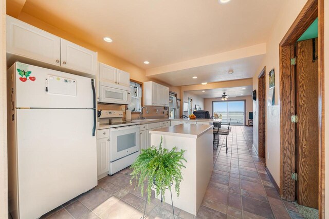 kitchen with recessed lighting, a peninsula, white cabinets, white appliances, and a sink