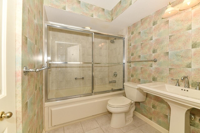 full bath with tile patterned flooring, tile walls, toilet, and bath / shower combo with glass door