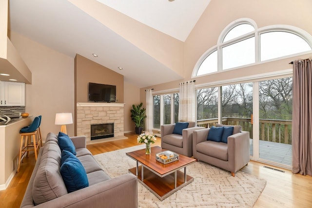 living room with a wealth of natural light, visible vents, a stone fireplace, and light wood-style floors