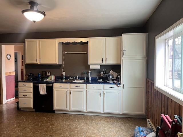 kitchen featuring a sink, black dishwasher, dark countertops, and wainscoting