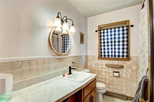 bathroom with toilet, vanity, wainscoting, tile patterned floors, and tile walls