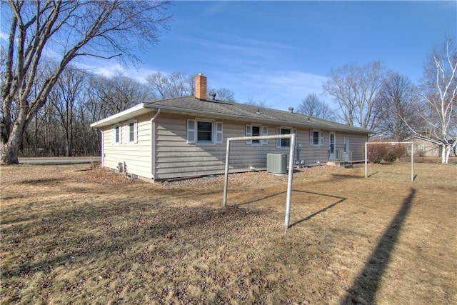 back of property featuring central air condition unit, a lawn, and a chimney