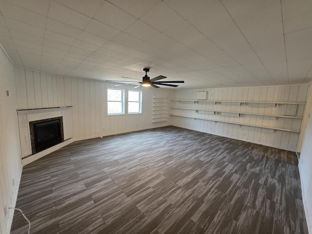 unfurnished living room featuring dark wood-type flooring, a wall unit AC, a fireplace, and ceiling fan