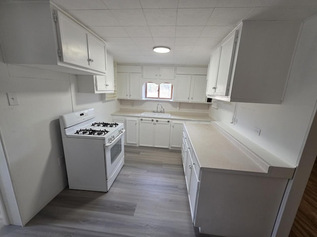 kitchen featuring dark wood-style floors, a sink, light countertops, white cabinetry, and white gas range