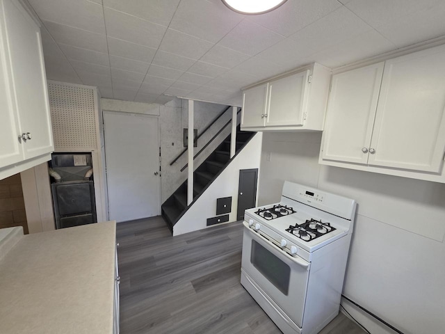 kitchen featuring white range with gas stovetop, wood finished floors, light countertops, and white cabinetry