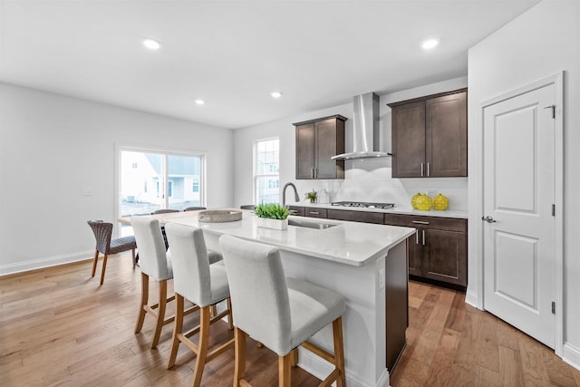 1251 Denmark Cir, Oregon, WI 53575 - kitchen featuring light wood-type flooring, a sink, stainless steel gas stovetop, a breakfast bar area, and wall chimney range hood