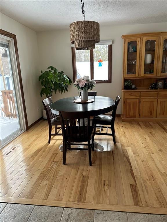 dining area featuring baseboards, visible vents, light wood-type flooring, and a textured ceiling