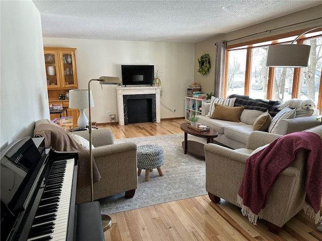 living room featuring a fireplace, light wood-style floors, baseboards, and a textured ceiling