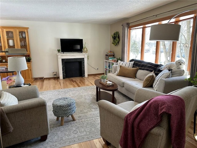 living room featuring wood finished floors, baseboards, visible vents, a fireplace, and a textured ceiling