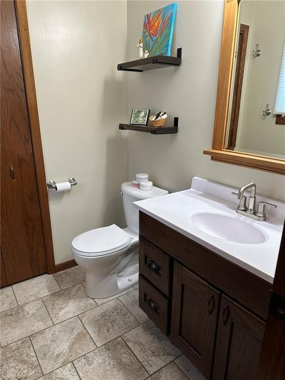 half bath with vanity, stone tile floors, toilet, and baseboards