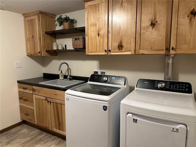 washroom featuring a sink, washer and dryer, a textured ceiling, cabinet space, and baseboards