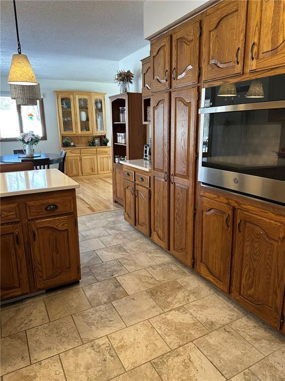 kitchen with brown cabinetry, oven, pendant lighting, stone finish floor, and a textured ceiling