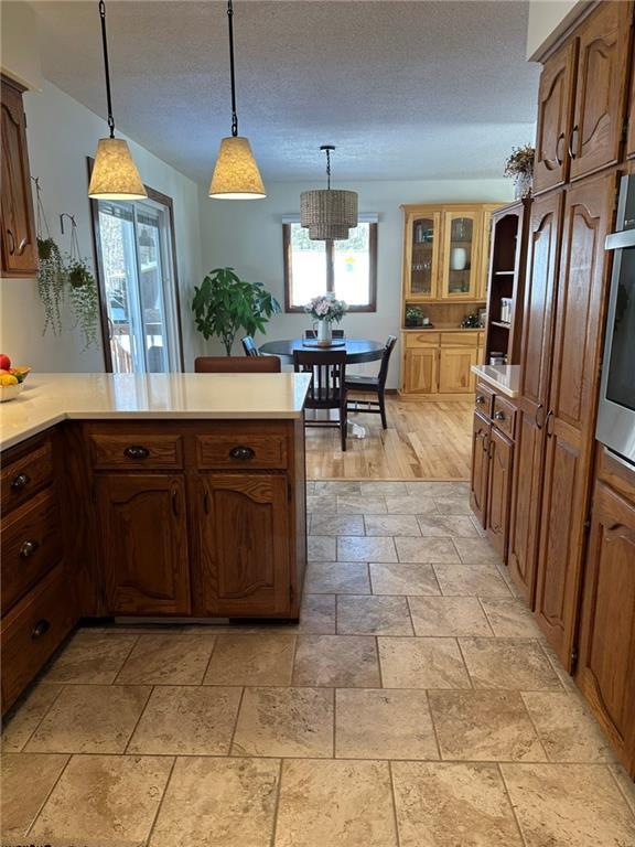 kitchen featuring decorative light fixtures, a peninsula, light countertops, and oven