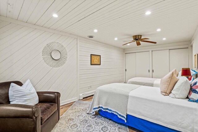 bedroom featuring two closets, visible vents, baseboard heating, wood finished floors, and wooden ceiling