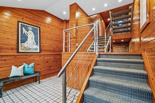 stairway featuring wooden walls, carpet, and vaulted ceiling