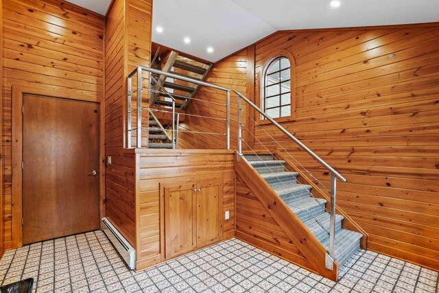 staircase featuring wooden walls, a baseboard heating unit, and lofted ceiling