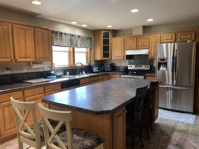 kitchen with a sink, under cabinet range hood, appliances with stainless steel finishes, a kitchen bar, and dark countertops