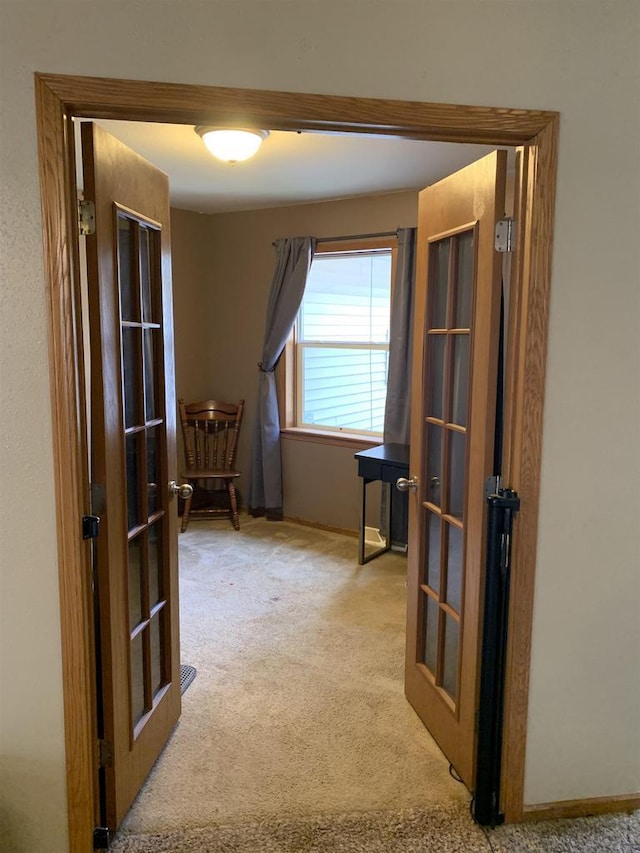 hall with french doors, baseboards, and light colored carpet