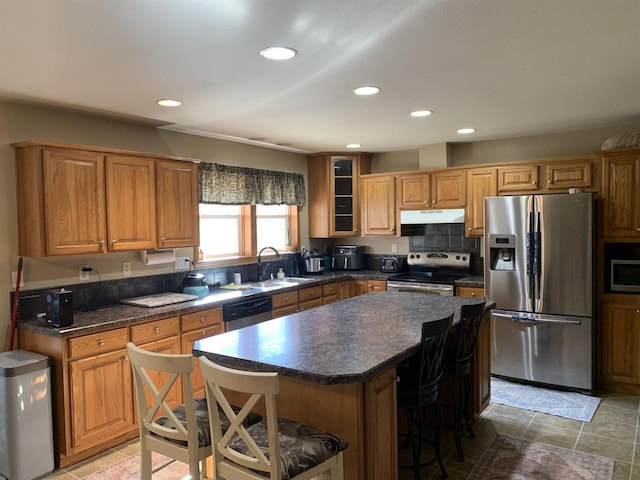 kitchen featuring dark countertops, under cabinet range hood, a kitchen breakfast bar, stainless steel appliances, and a sink