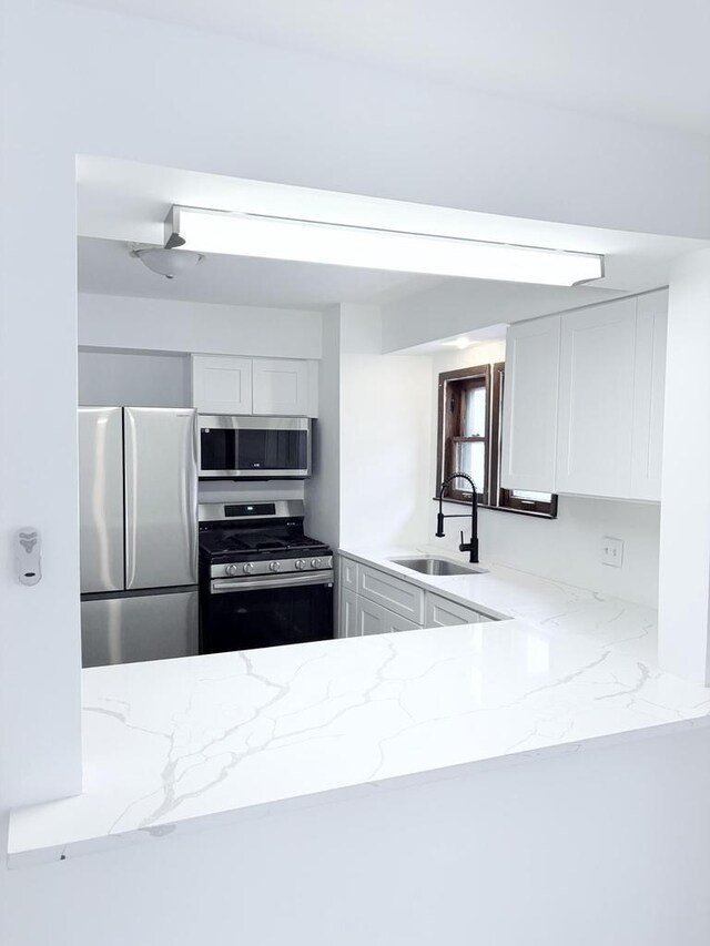 kitchen with white cabinetry, appliances with stainless steel finishes, light stone countertops, and a sink