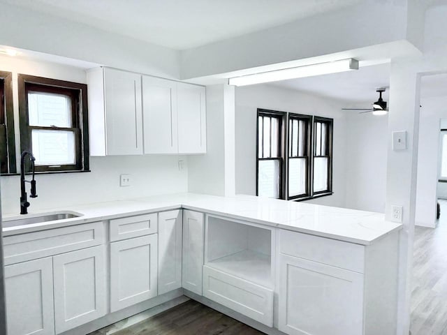kitchen with a ceiling fan, dark wood finished floors, a peninsula, a sink, and white cabinetry