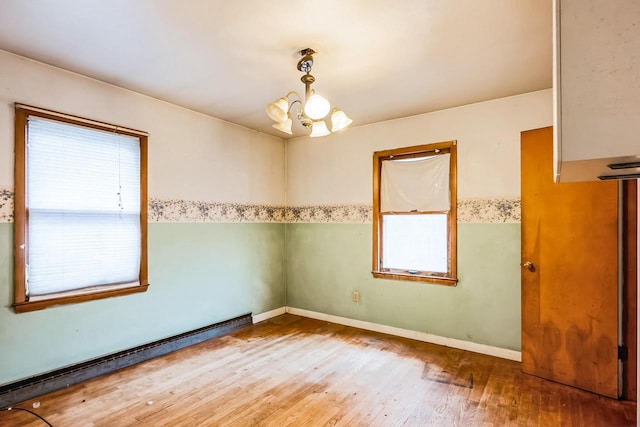 empty room with baseboards, wood finished floors, baseboard heating, and a chandelier