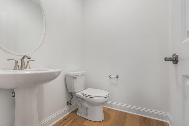bathroom with toilet, wood finished floors, baseboards, and a sink