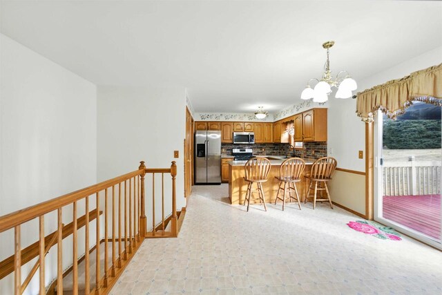 kitchen featuring backsplash, brown cabinets, a peninsula, an inviting chandelier, and stainless steel appliances