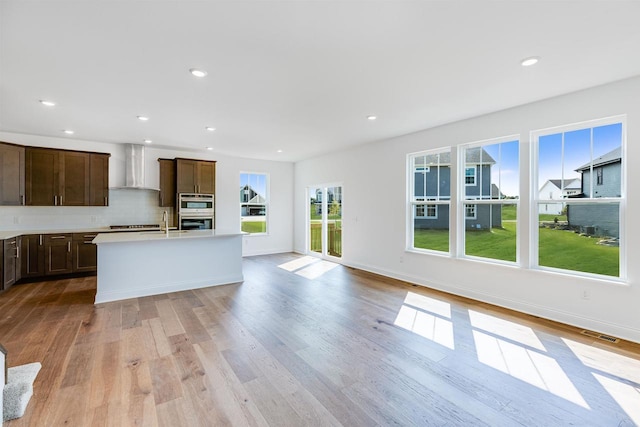 kitchen featuring visible vents, tasteful backsplash, stainless steel double oven, wall chimney exhaust hood, and dark brown cabinets