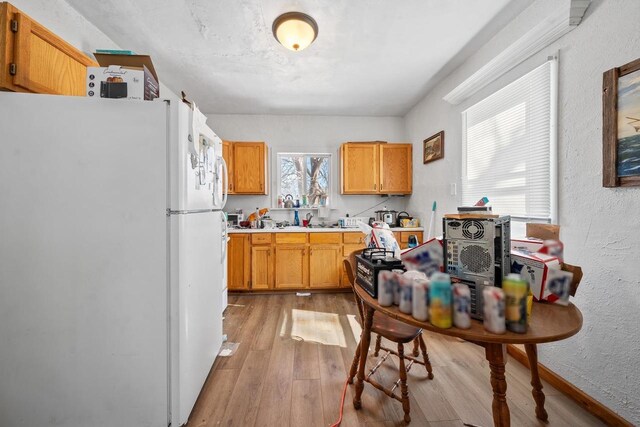 kitchen with light countertops, a textured wall, light wood-style floors, and freestanding refrigerator