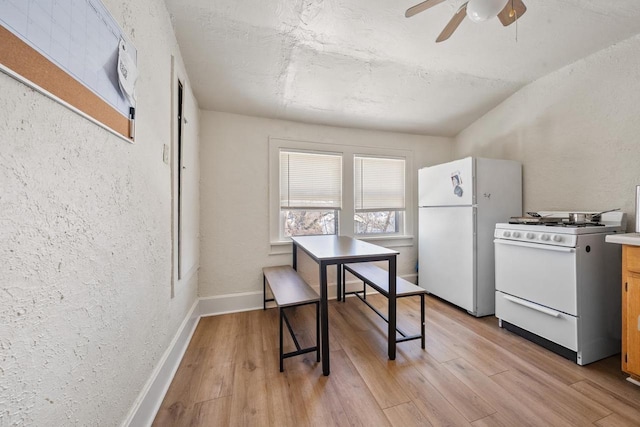 dining space with baseboards, light wood-style floors, a ceiling fan, and a textured wall