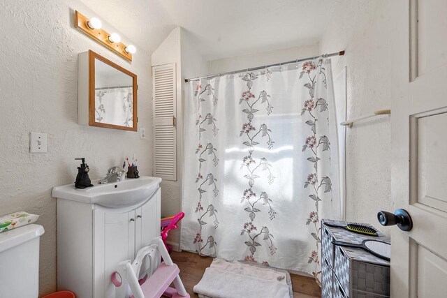 full bathroom featuring a shower with curtain, toilet, wood finished floors, vanity, and a textured wall
