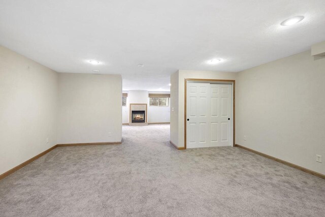 unfurnished room featuring carpet, baseboards, and a warm lit fireplace