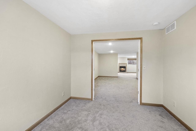 empty room with visible vents, light colored carpet, baseboards, and a warm lit fireplace