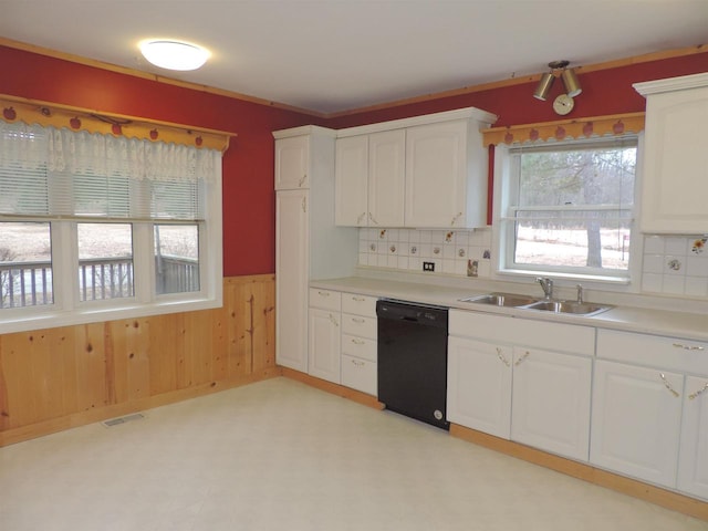 kitchen featuring wooden walls, black dishwasher, wainscoting, white cabinets, and a sink