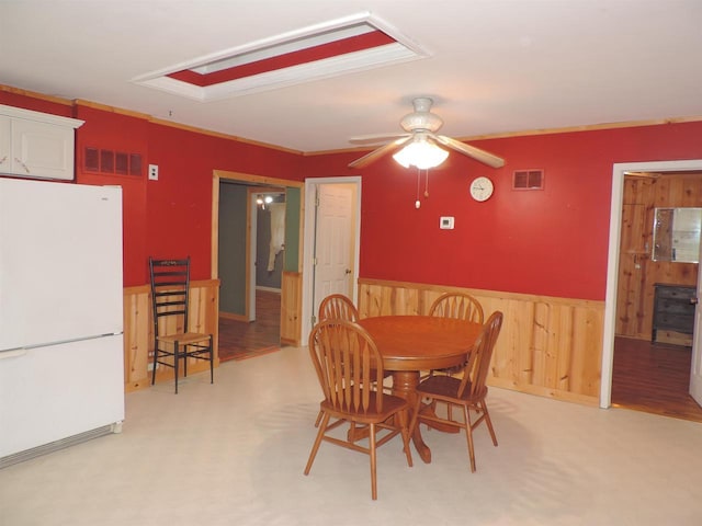 dining area featuring visible vents, light colored carpet, a ceiling fan, and a wainscoted wall