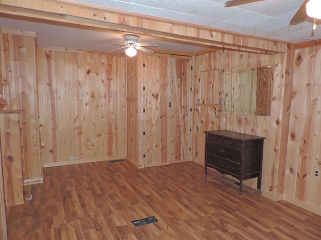 spare room with visible vents, wood walls, a ceiling fan, and wood finished floors