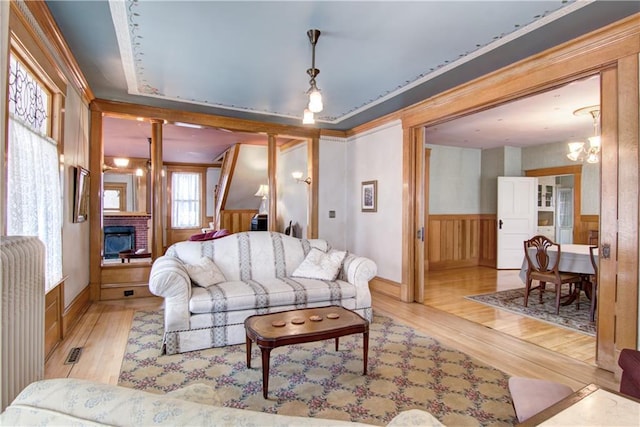 435 Jefferson St, Eau Claire, WI 54701 - living area featuring wood finished floors, wainscoting, a fireplace, a chandelier, and decorative columns