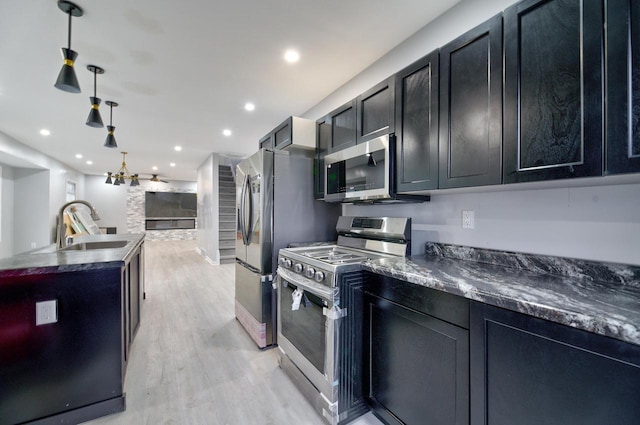 kitchen with a sink, appliances with stainless steel finishes, light wood finished floors, and dark cabinets