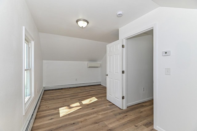 additional living space featuring a wall mounted air conditioner, baseboard heating, wood finished floors, and vaulted ceiling